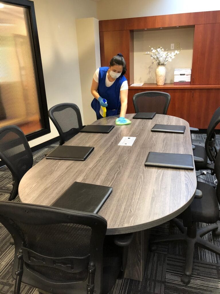 Office cleaning services staff member wiping a conference table during a professional office cleaning session
